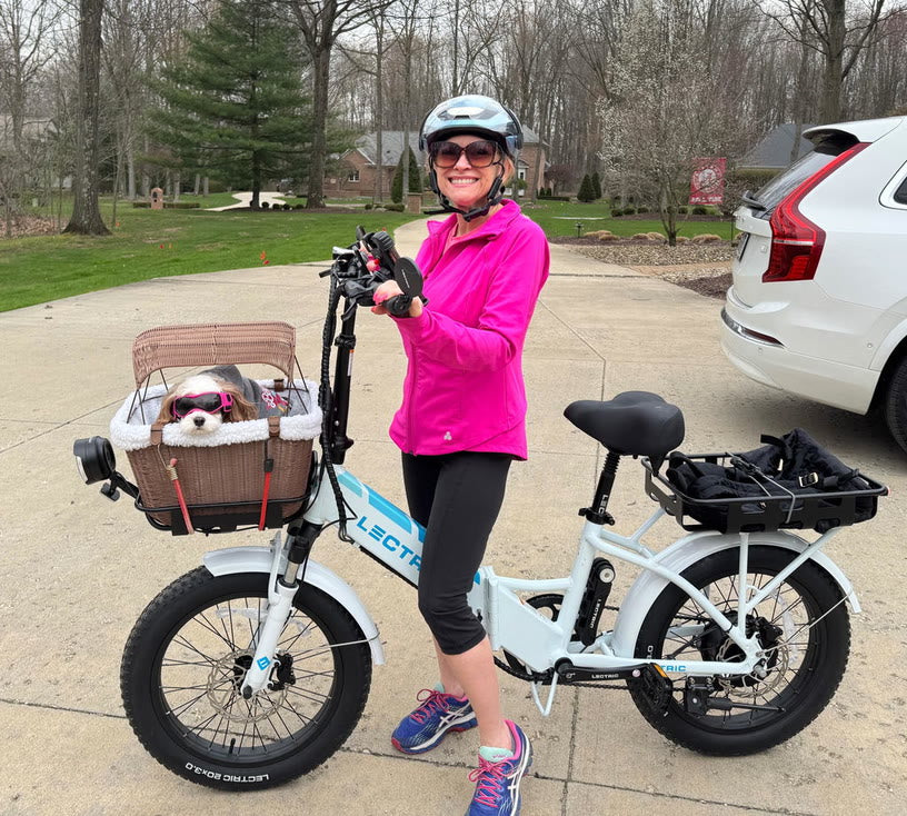 Customer photo: rider in a pink jacket beside her e-bike, with a dog in the front basket